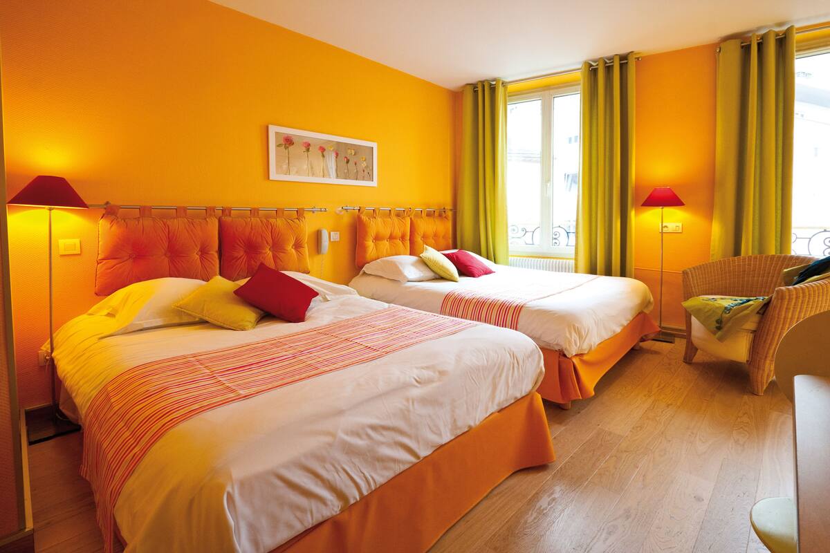 A hotel room with two beds, a chair, and a window with curtains.