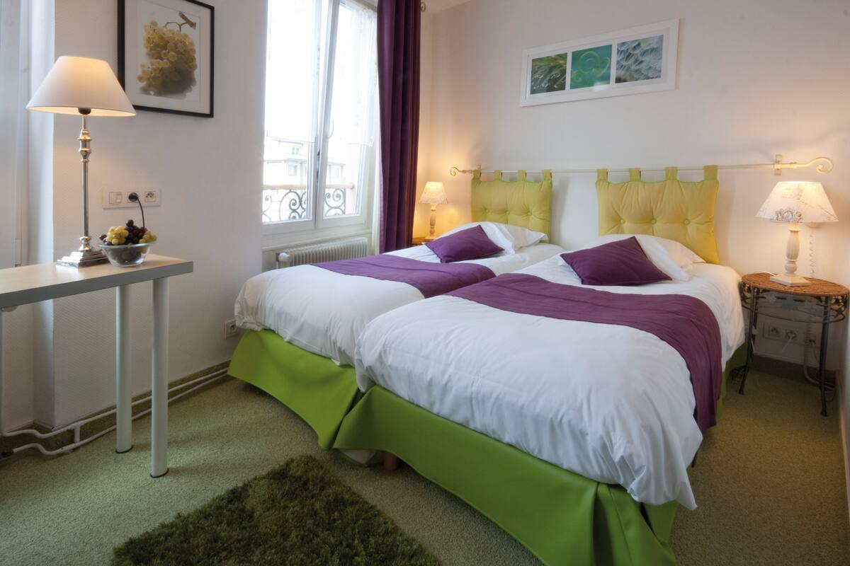A double bed with green and white bedding, a bedside table with a lamp, and a window with curtains.
