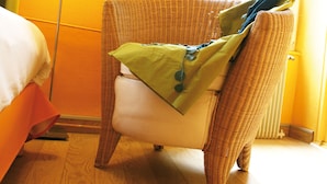 A wicker chair with a green pillow and a red lamp in a room with wooden flooring and yellow walls.