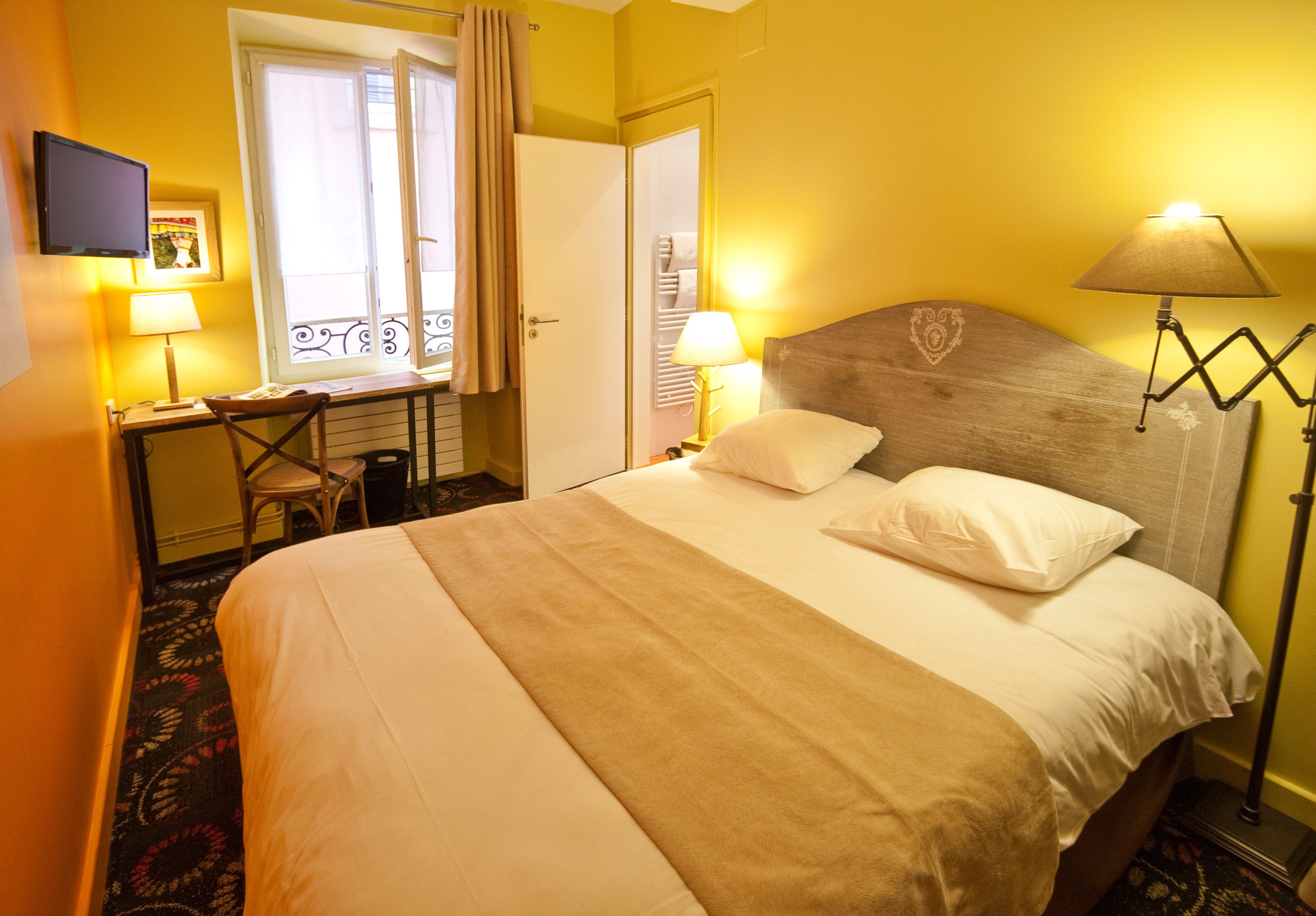 Habitación de hotel con cama, dos lámparas de noche, escritorio con silla, televisor y ventana con cortinas.