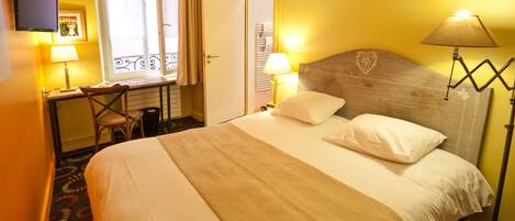 Habitación de hotel con cama, dos lámparas de noche, escritorio con silla, televisor y ventana con cortinas.