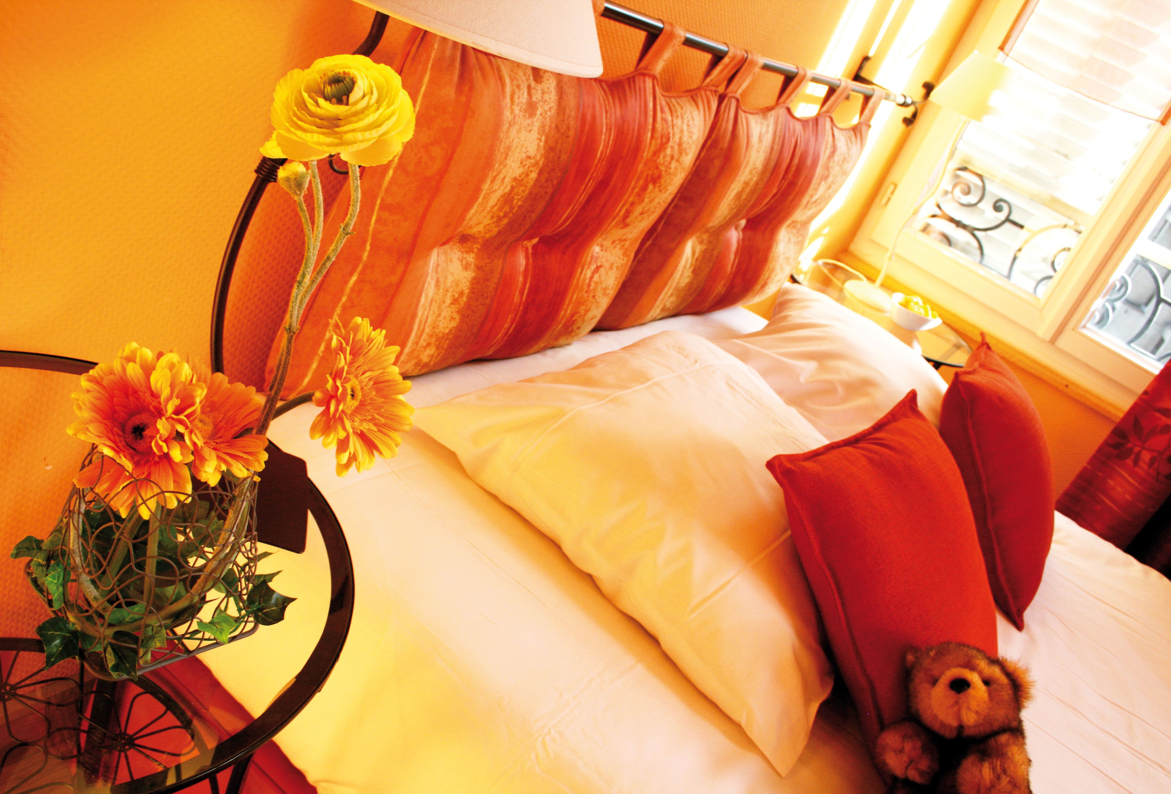 A bed with white linens, a teddy bear, and a vase with flowers.