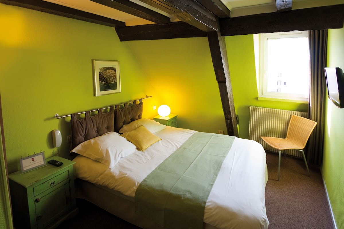 A hotel room with a bed, a chair, a nightstand with a phone, and a window with curtains.