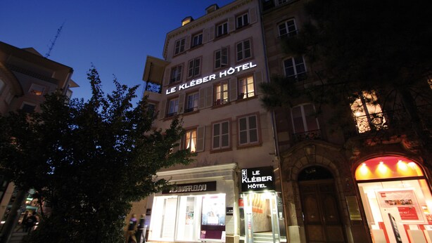 A hotel with a classic European facade, illuminated signage, and a cobblestone street.