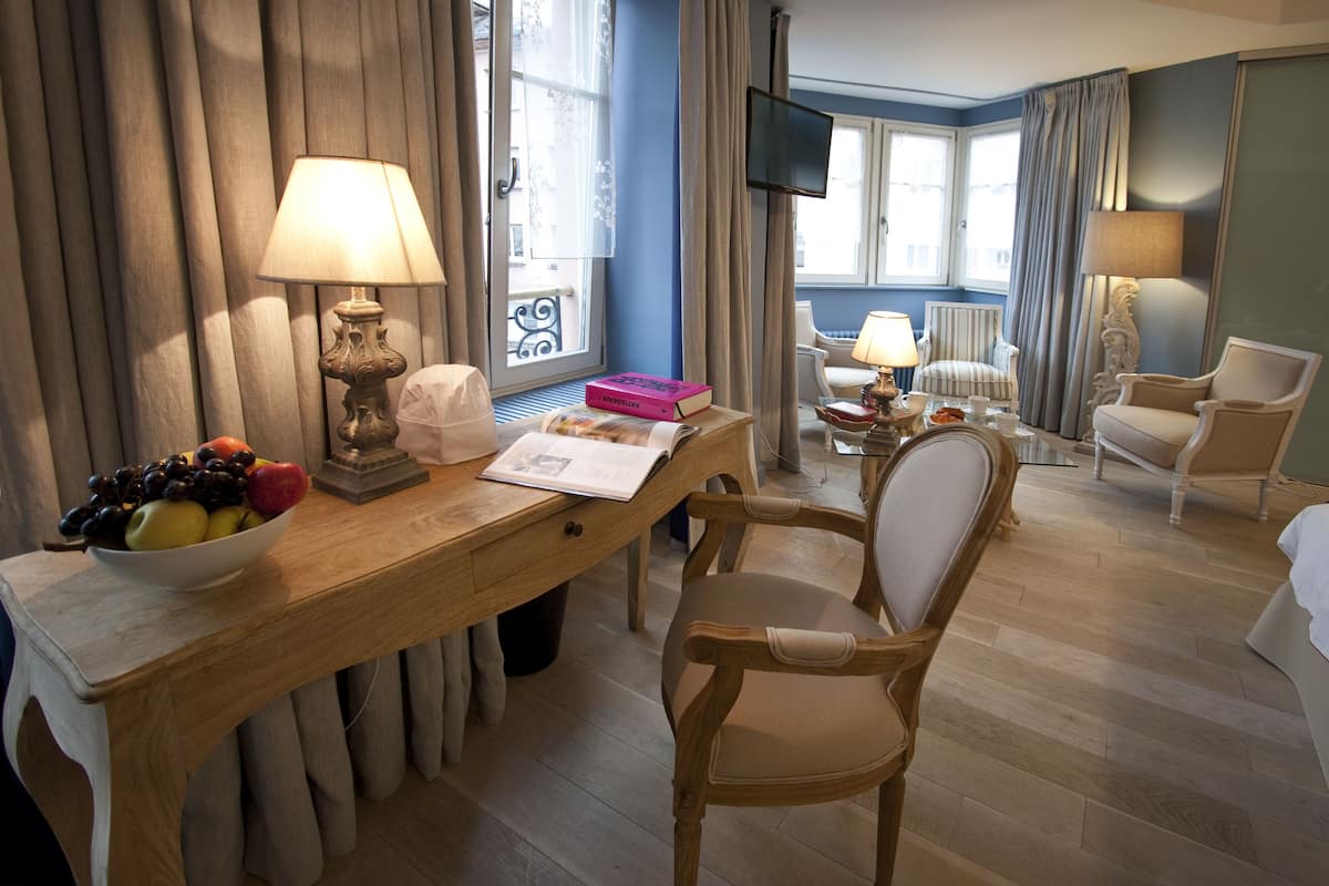 A hotel room with a wooden desk, a chair, a TV, and a window with curtains.