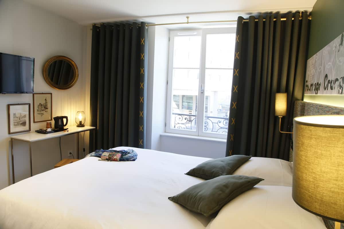 A hotel room with a large bed, a desk with a lamp, a television, and a window with curtains.