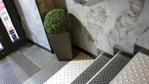 A staircase with metal steps and a handrail, a potted plant, and a textured wall.