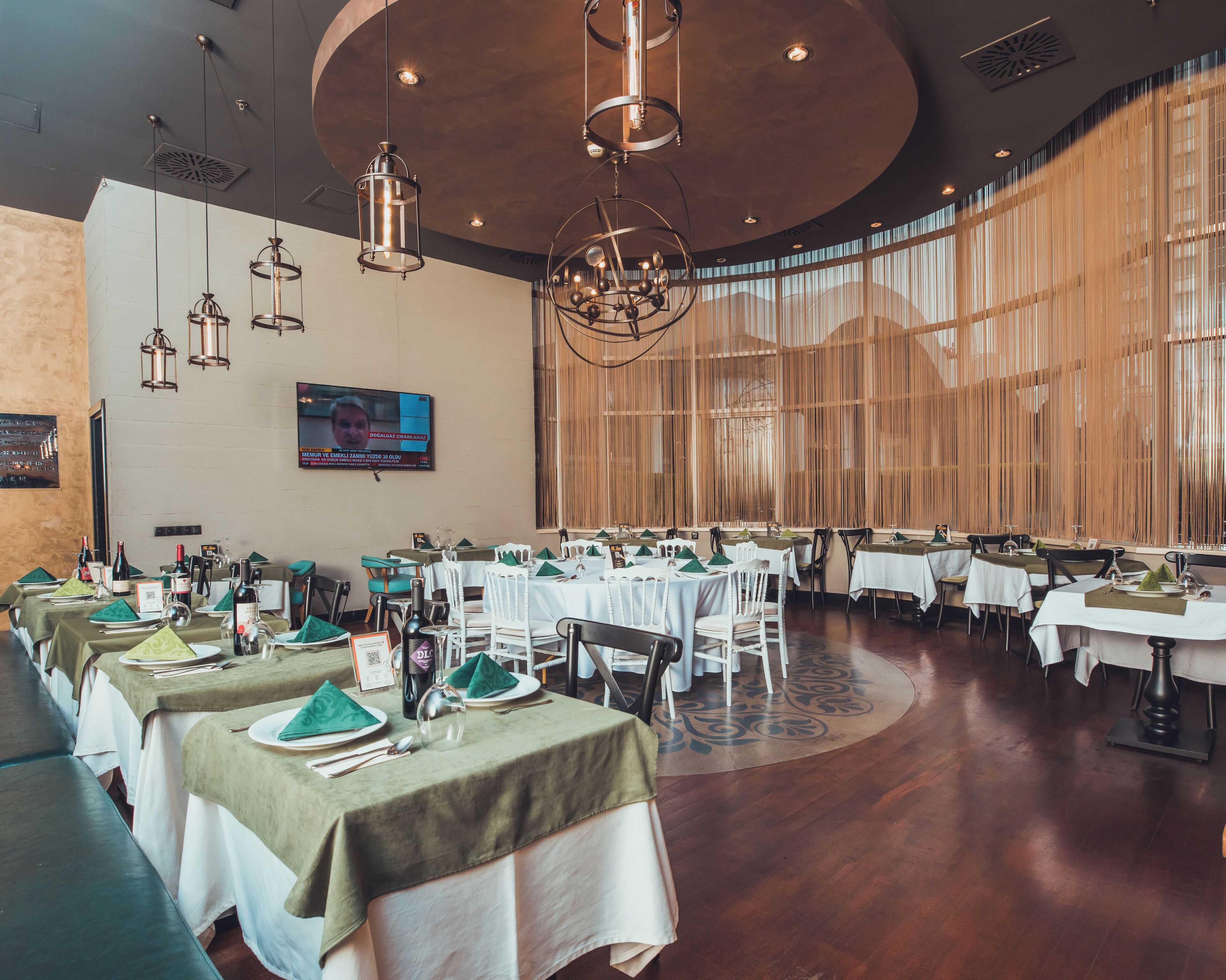 A restaurant with round tables, green tablecloths, and hanging pendant lights.