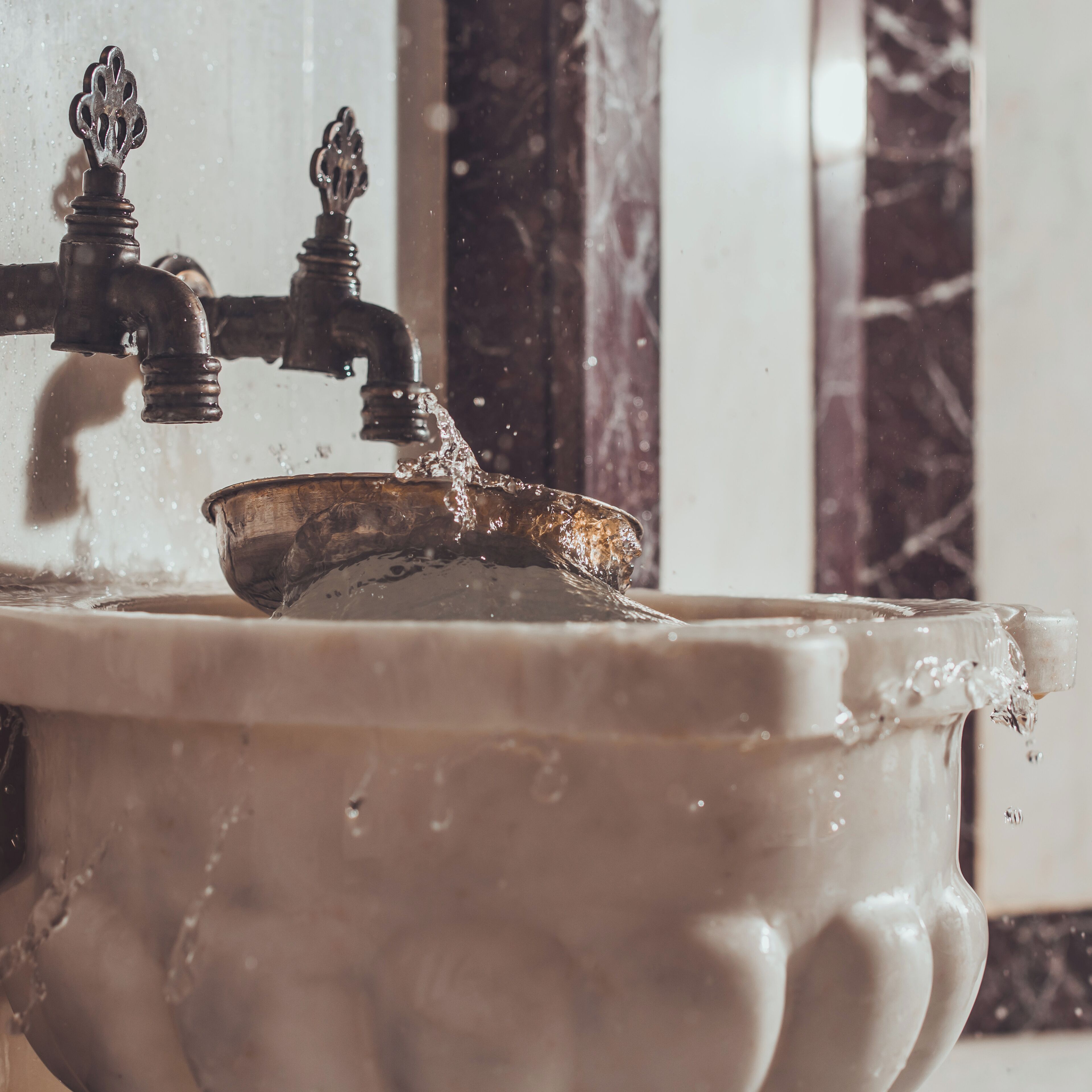 Un lavabo de estilo antiguo con agua corriente, un recipiente metálico y un diseño de grifo clásico.