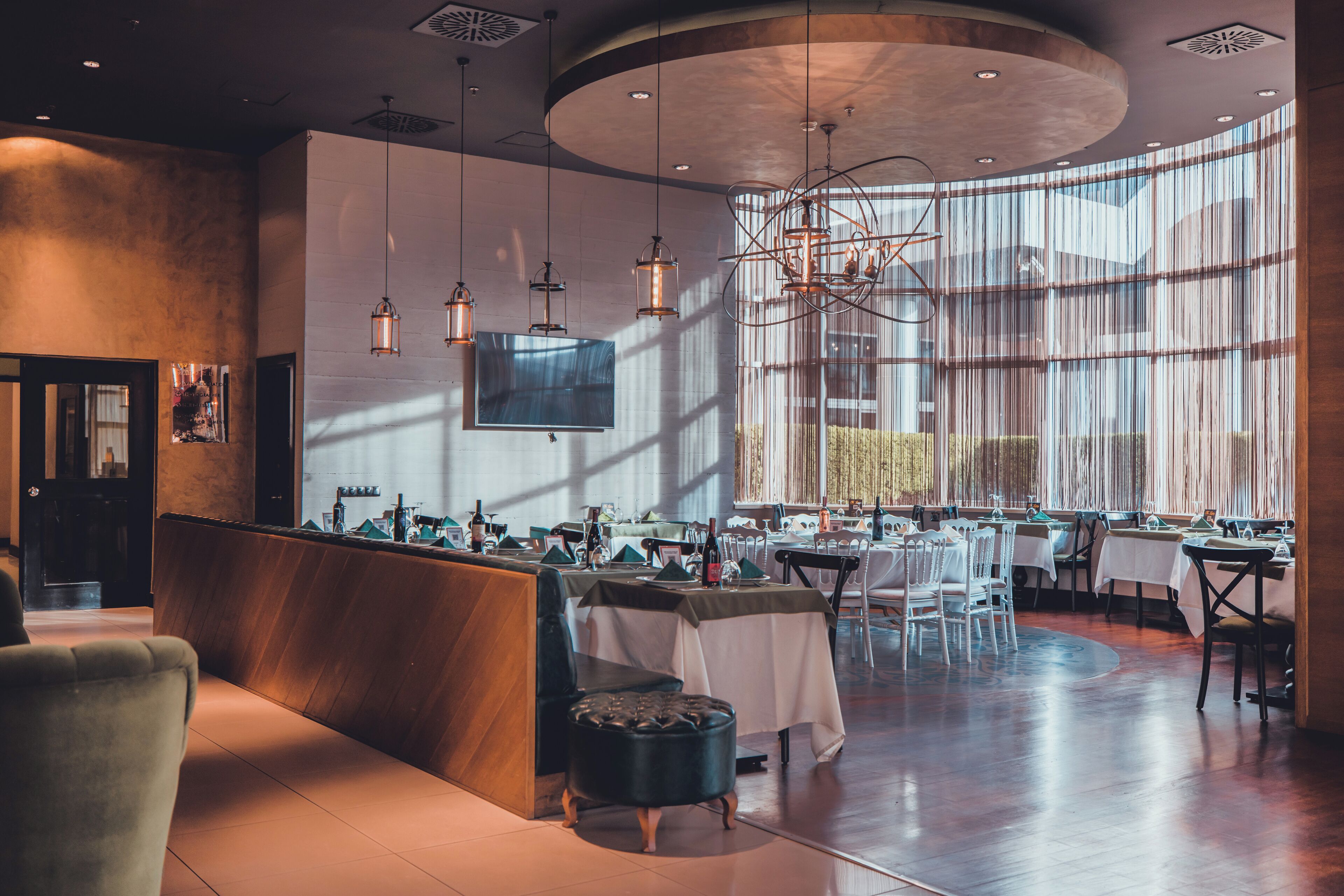 A modern restaurant interior with a central seating area, multiple tables, and a large window providing natural light.