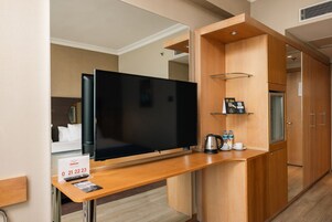 Ein modernes Hotelzimmer mit Flachbildfernseher, Schreibtisch aus Holz mit Kaffeemaschine und Minibar.