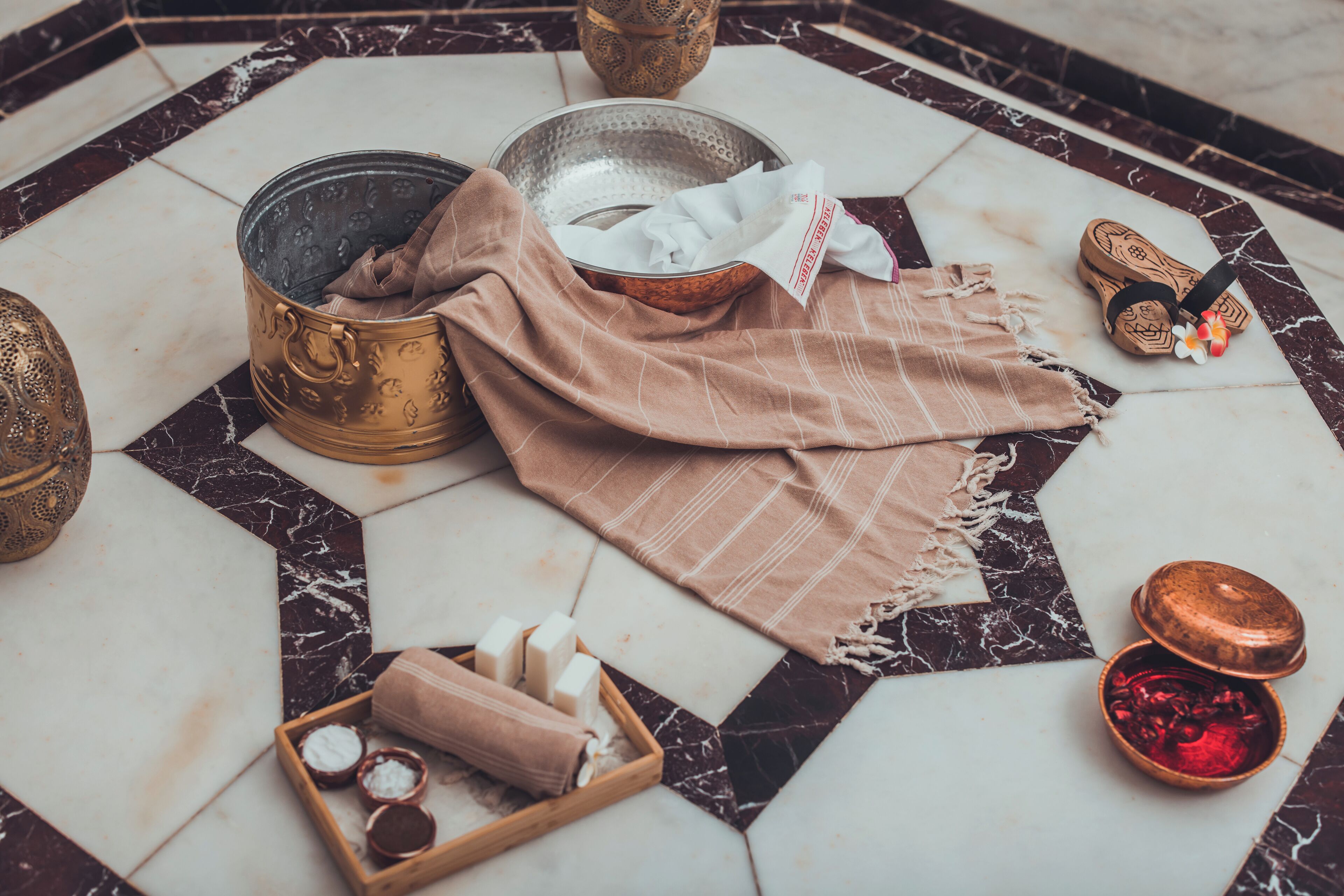 A bathroom with a marble floor, a copper basin, a wooden tray with soap, and a towel.