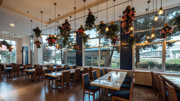 A spacious restaurant with wooden tables and chairs, large windows, and hanging floral decorations. - WOW Airport Hotel (Istanbul)