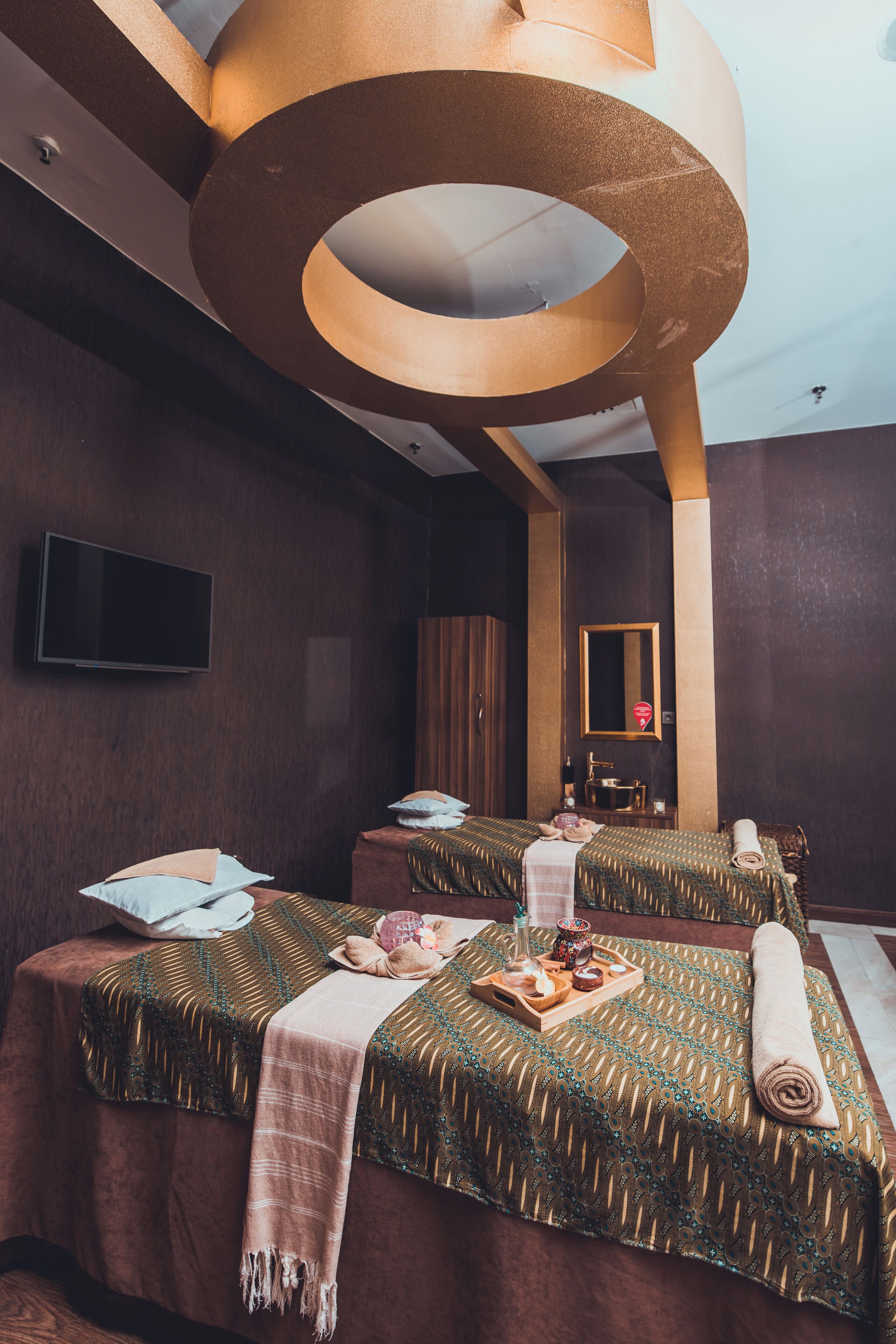 Habitación de hotel con dos camas, televisión, espejo y un elemento decorativo circular en el techo.
