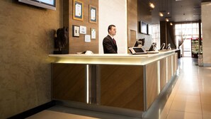 A modern reception desk with a digital screen, framed certificates, and a man standing behind it. - WOW Airport Hotel (Istanbul)