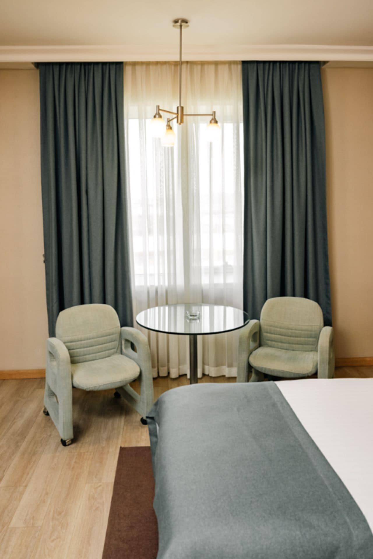 Een hotelkamer met een bed, twee fauteuils, een kleine ronde tafel en een kroonluchter.