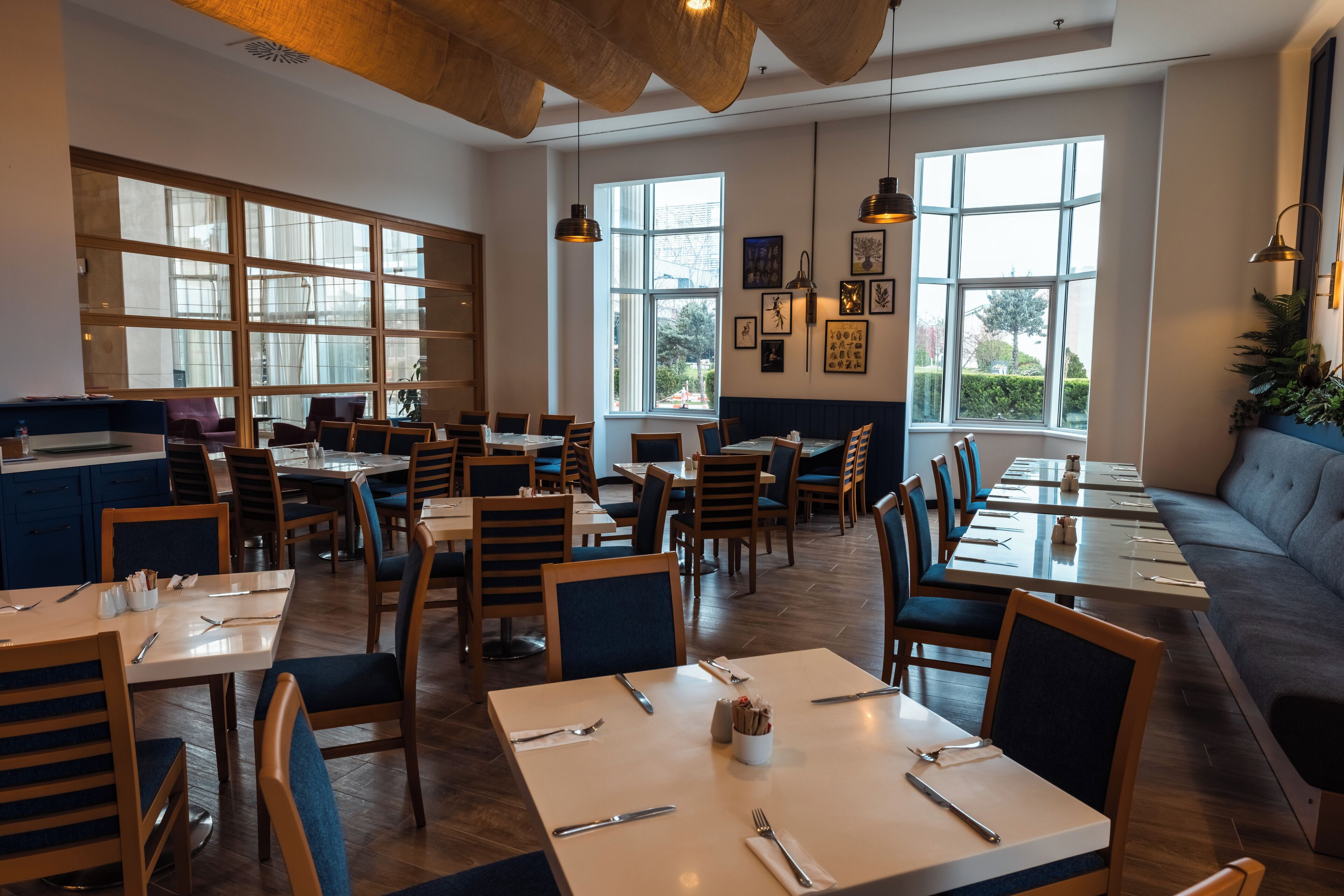 Un restaurante con mesas y sillas de madera, ventanas amplias y un banco acolchado azul.