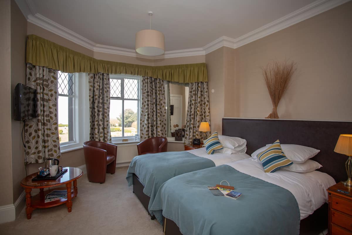 A hotel room with two beds, a sitting area with a chair, a table, and a television.