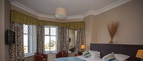 A hotel room with two beds, a sitting area with a chair, a table, and a television.