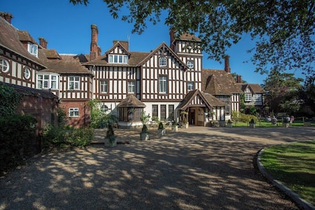 A traditional Tudor-style building with a symmetrical facade, multiple chimneys, and a central entrance with a covered porch.