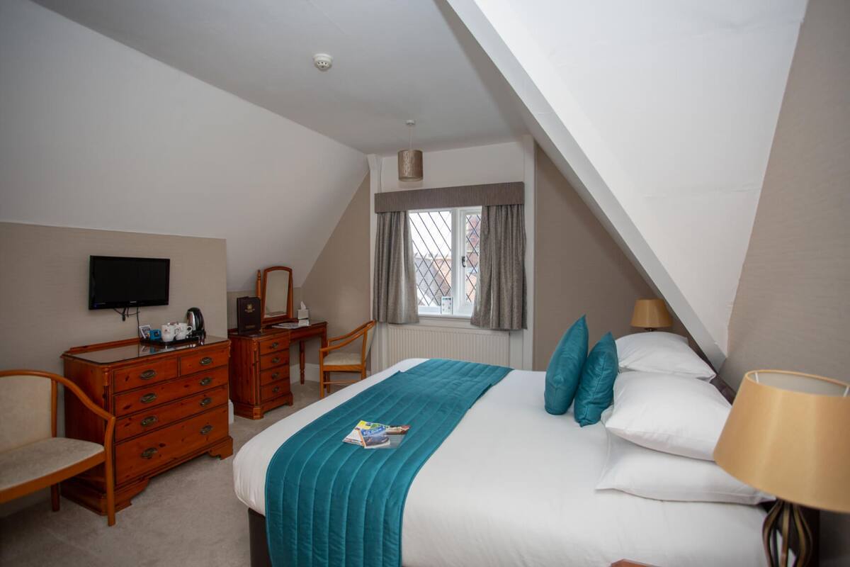 A bedroom with a bed, a dresser, a chair, a television, and a window with curtains.
