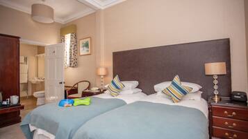 A hotel room with two beds, a nightstand, a lamp, a dresser, and a bathroom visible through an open door.