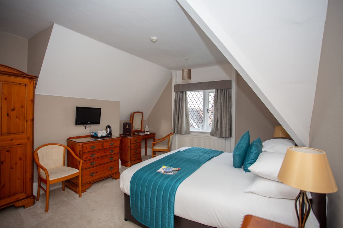 A bedroom with a bed, a dresser, a desk, a chair, a television, and a window with curtains.
