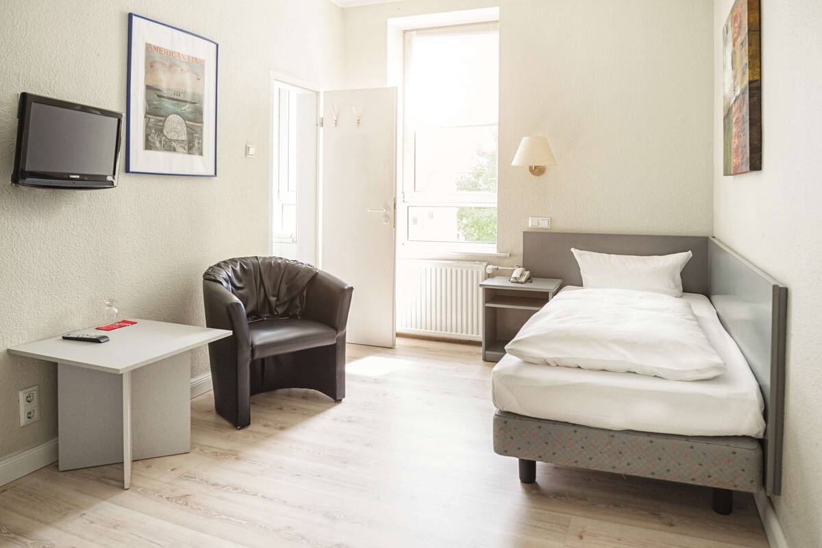 Ein Hotelzimmer mit Bett, Schreibtisch, Stuhl, Fernseher und Fenster.