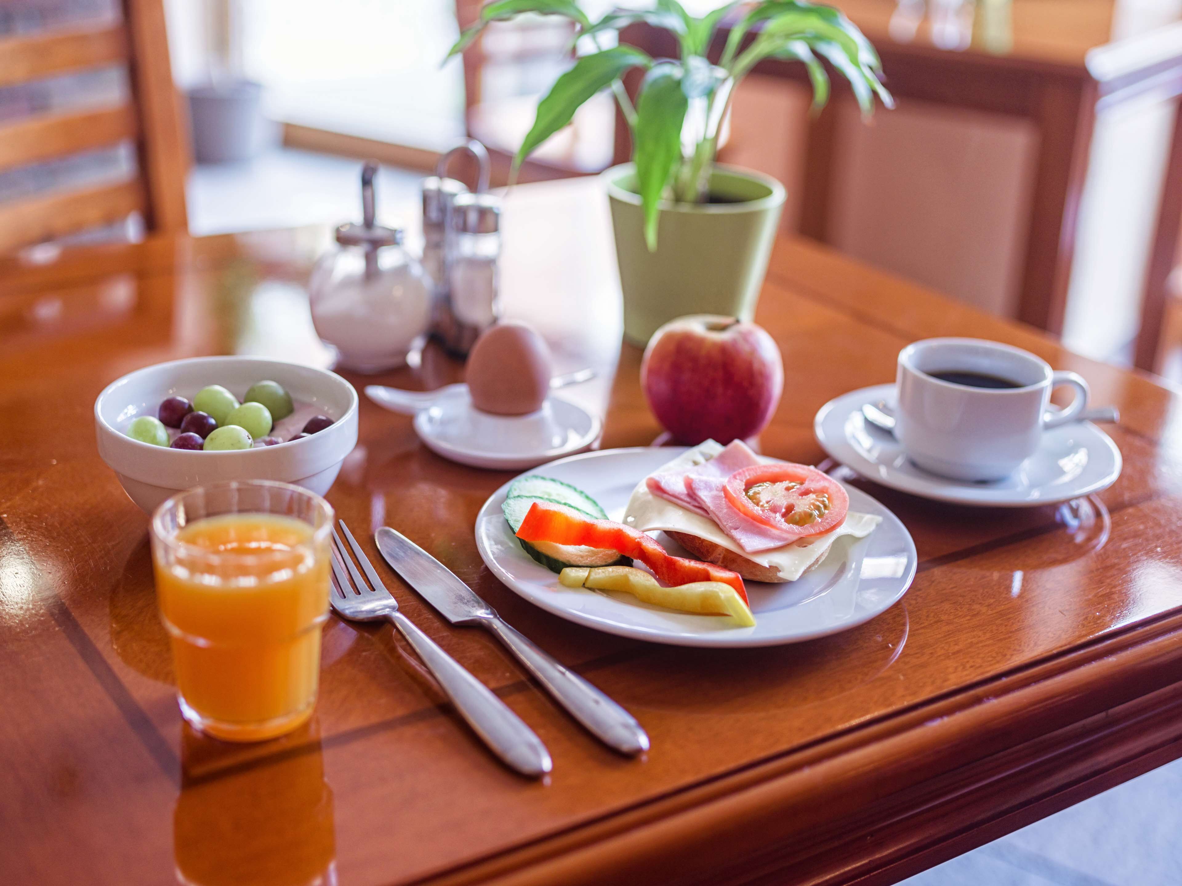 A breakfast table with a bowl of fruit, a glass of orange juice, a plate with eggs, a cup of coffee, and a plant.