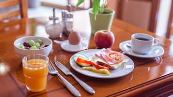 A breakfast table with a bowl of fruit, a glass of orange juice, a plate with eggs, a cup of coffee, and a plant.