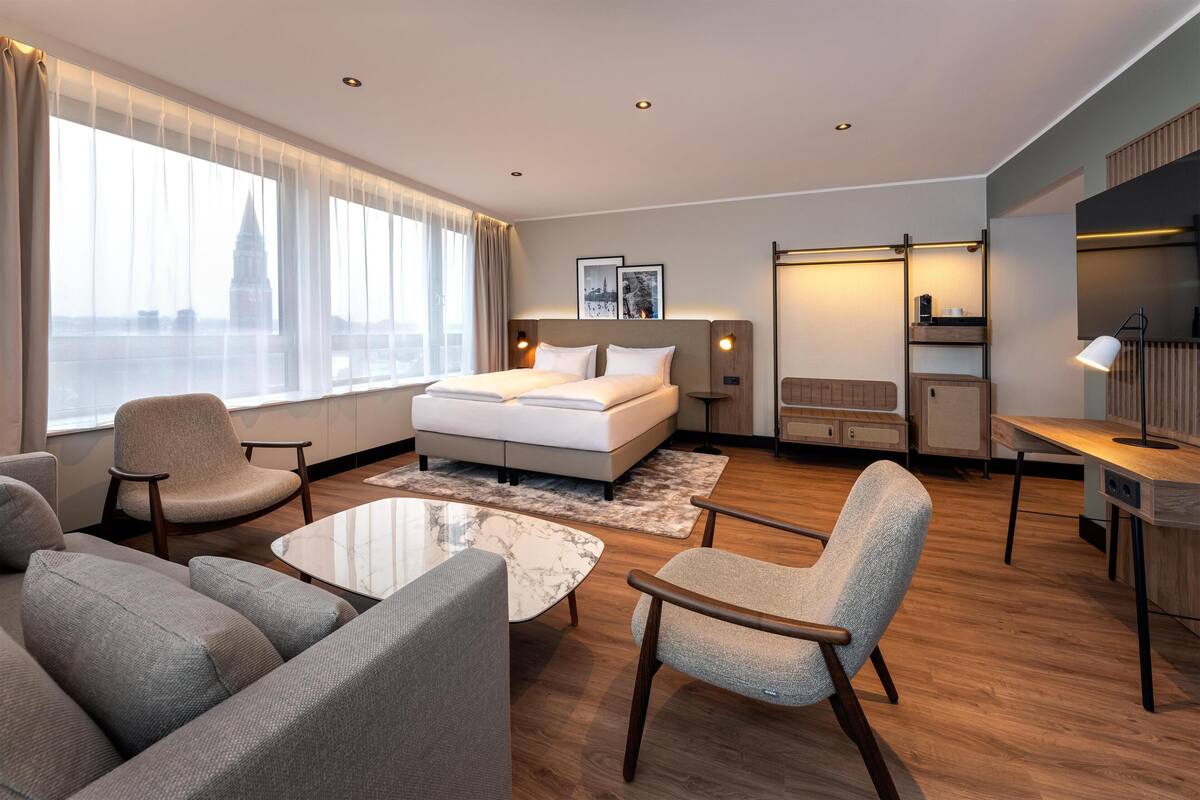 A modern hotel room with a large bed, a sofa, a coffee table, and a desk.