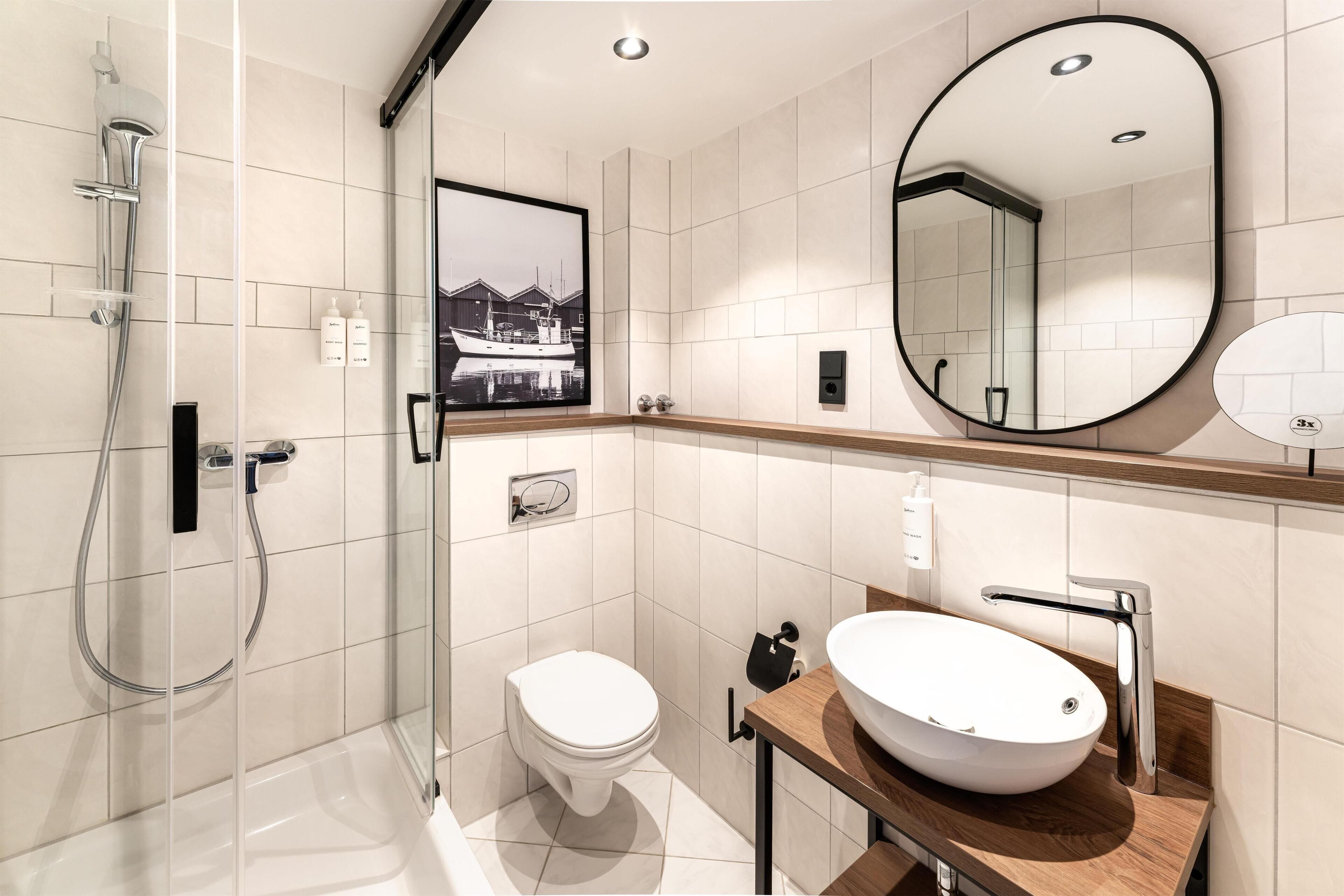 A modern bathroom with a glass-enclosed shower, a white toilet, a large oval sink, and a mirror.