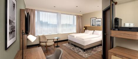 A hotel room with a bed, desk, chair, and a large window.