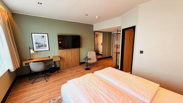 Habitación de hotel con cama, escritorio, silla, televisor y un baño pequeño.
