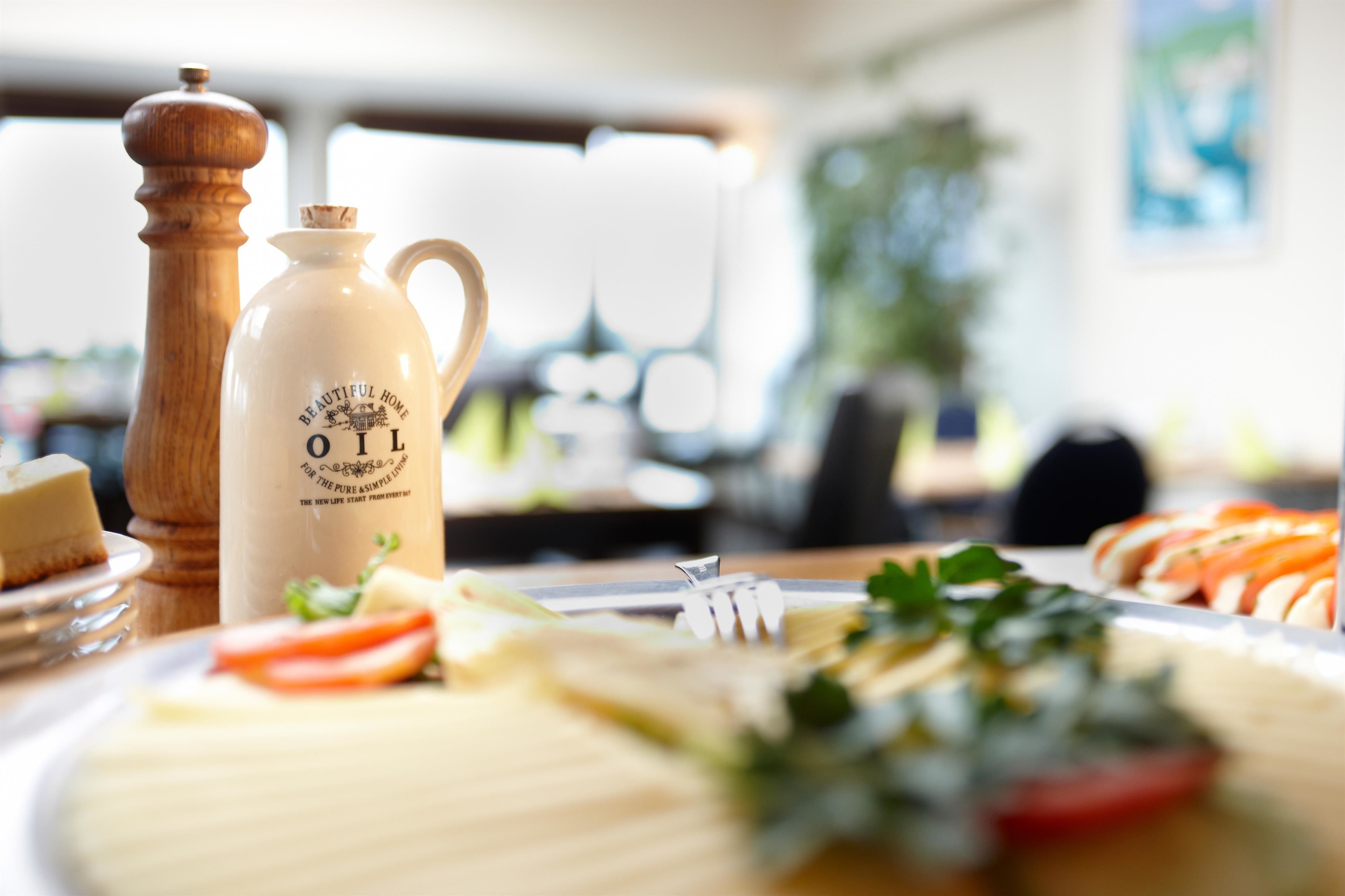 Una mesa con una botella etiquetada como 'Beautiful Home Oil', un molinillo de pimienta y diversos alimentos.