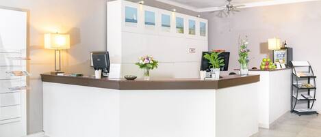 Un área de recepción con mostrador, una lámpara, una computadora y una pared con cuadros enmarcados.