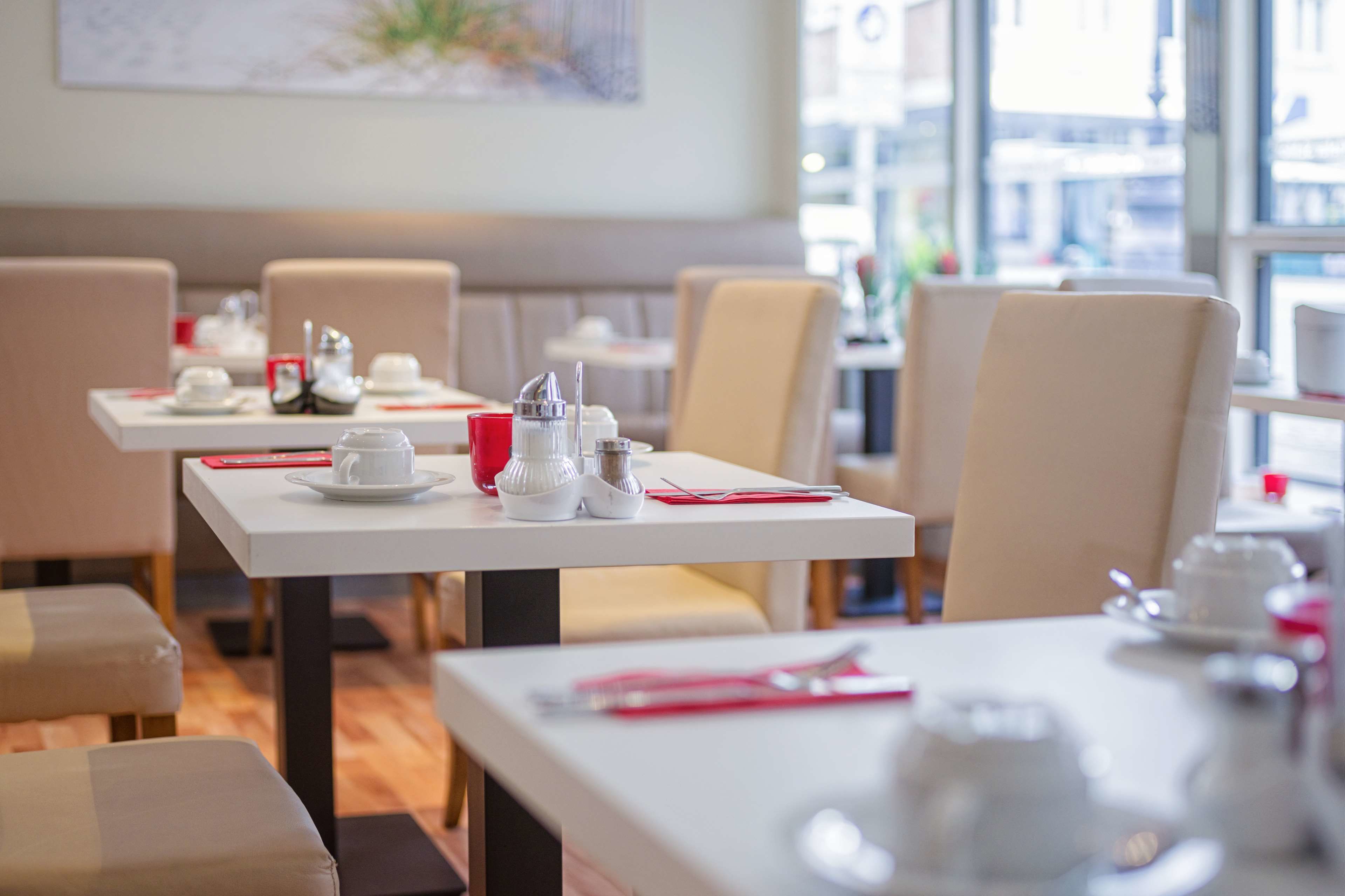Un espace repas avec des tables préparées pour deux personnes, chacune étant recouverte d’une nappe blanche, agrémentée de serviettes rouges et de couverts en argent.