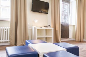 A modern room with a white table and blue cushioned seating, a flat-screen TV on the wall, and a radiator.