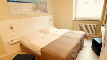 A double bed with a headboard, a bedside table with a lamp, a radiator, and a window with curtains.