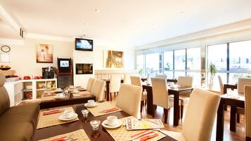 A hotel dining area with multiple tables, chairs, and a television mounted on the wall.