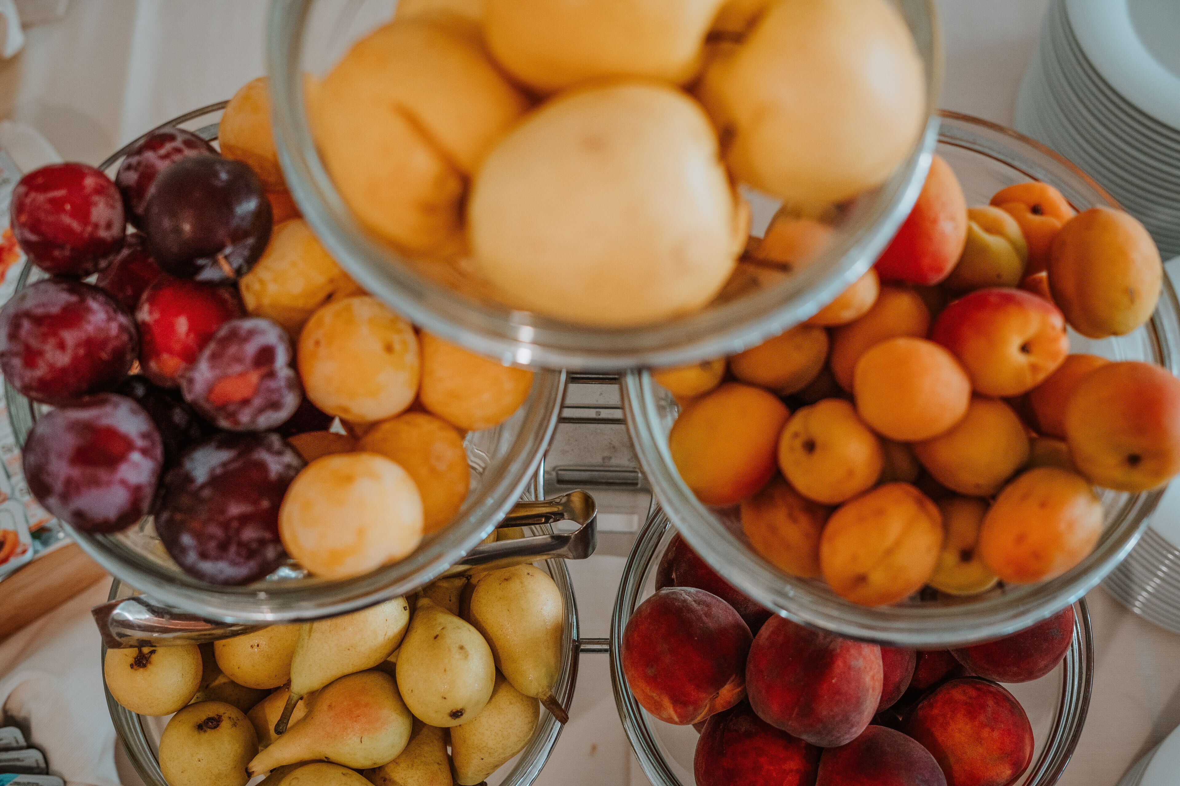A buffet with multiple bowls of fruits including plums, pears, and peaches.