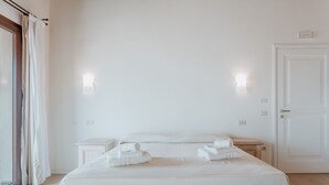 Una habitación de hotel minimalista con una cama grande, dos mesitas de noche y una puerta.
