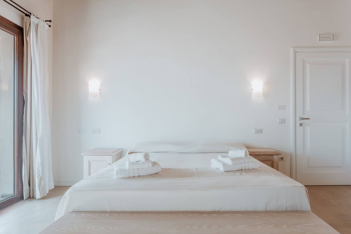 A minimalist hotel room with a large bed, two bedside tables, and a door.