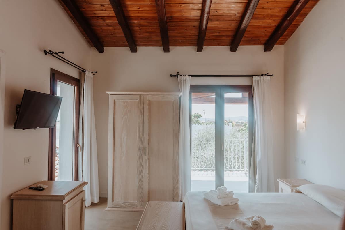 A bedroom with a wooden ceiling, a bed with towels, a TV, and a balcony view.