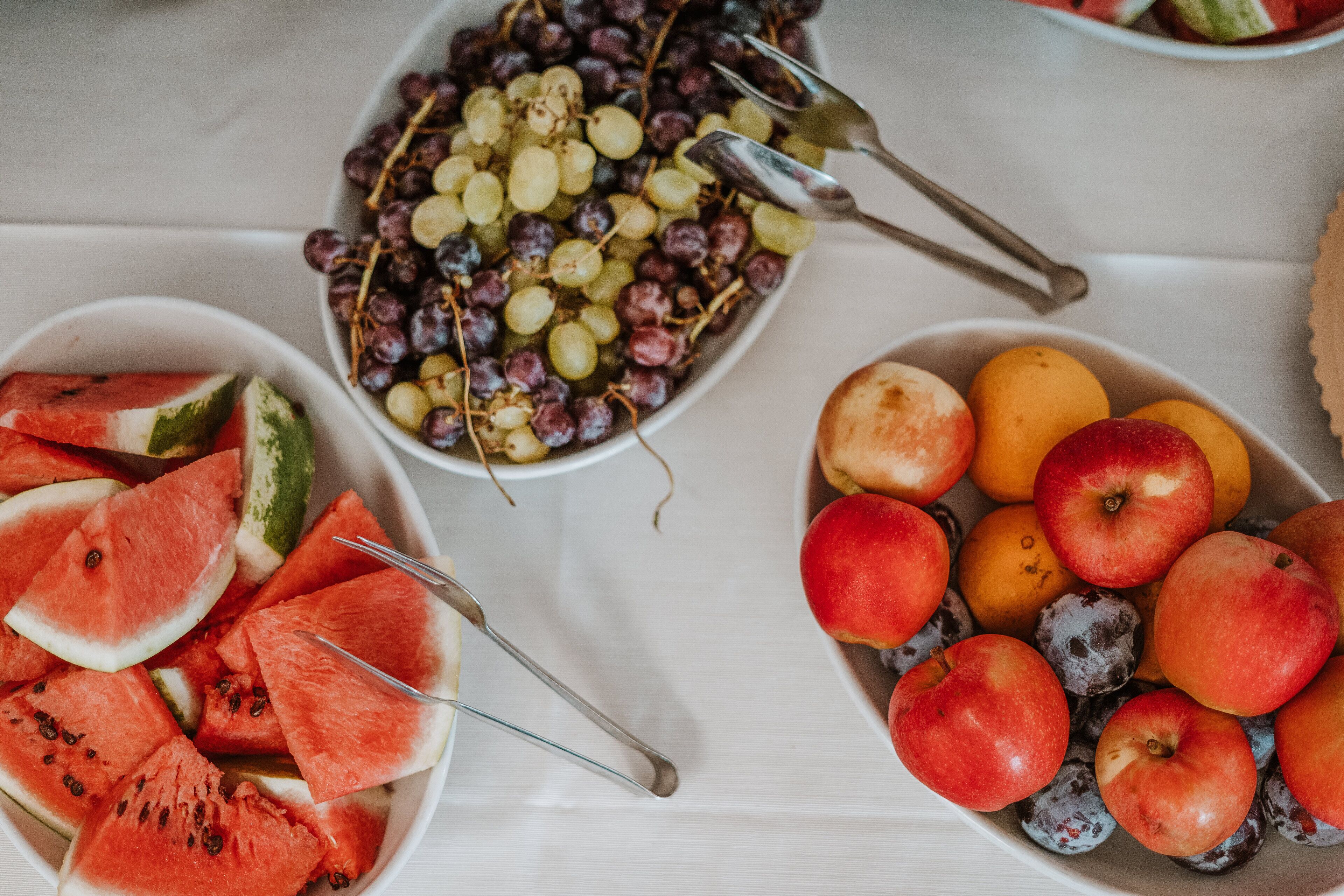 A table with bowls of watermelon, grapes, and various fruits.