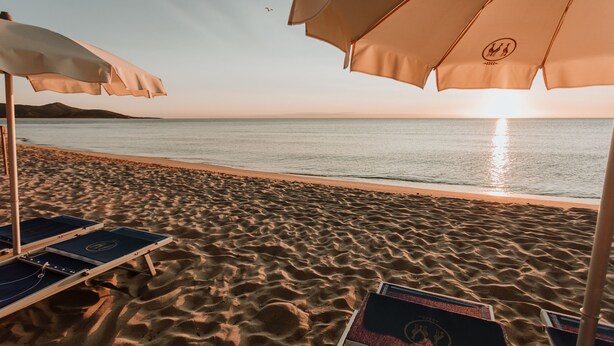 Una playa con tumbonas y sombrillas, cielo despejado y el océano al fondo.