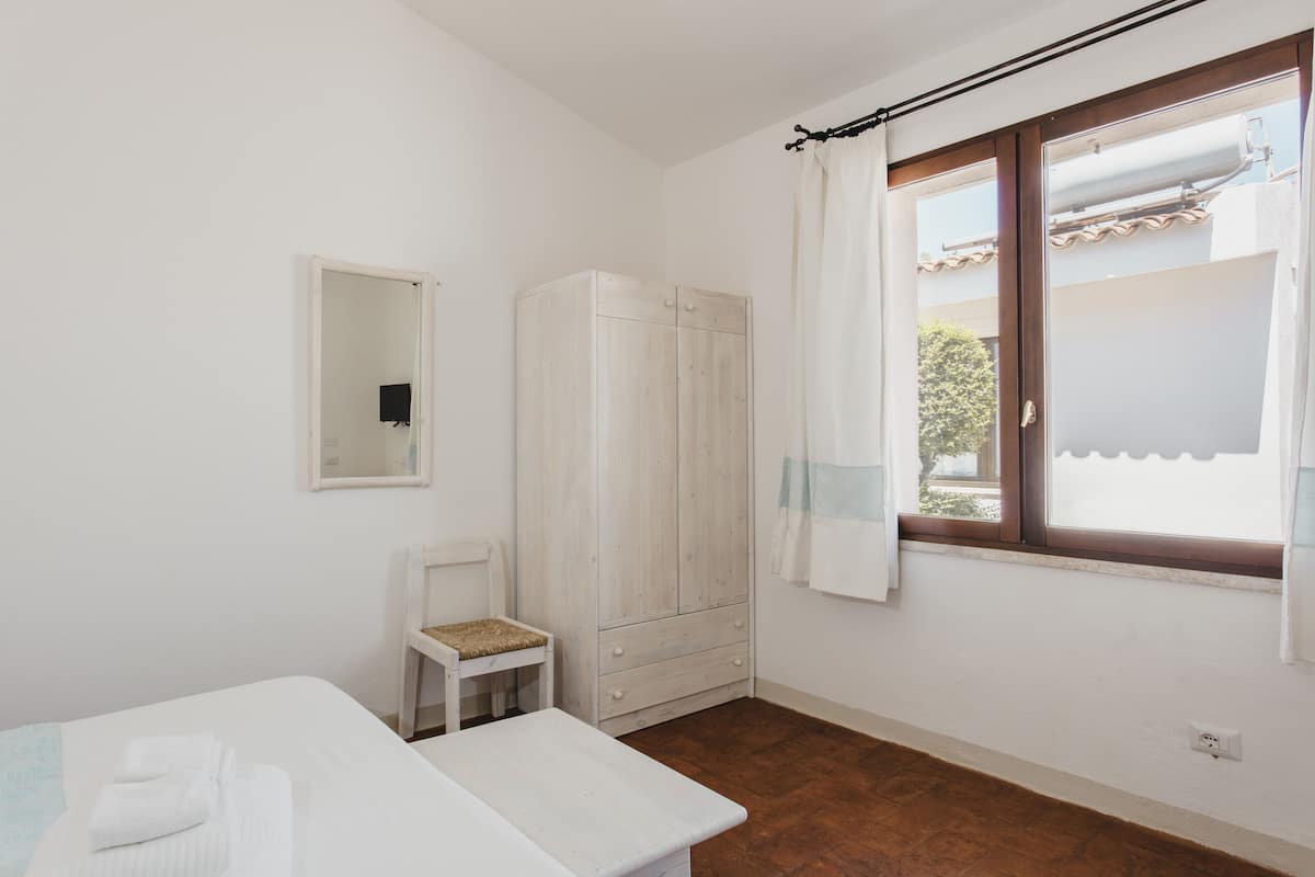 A room with a bed, a small table, a chair, a wardrobe, and a window with curtains.