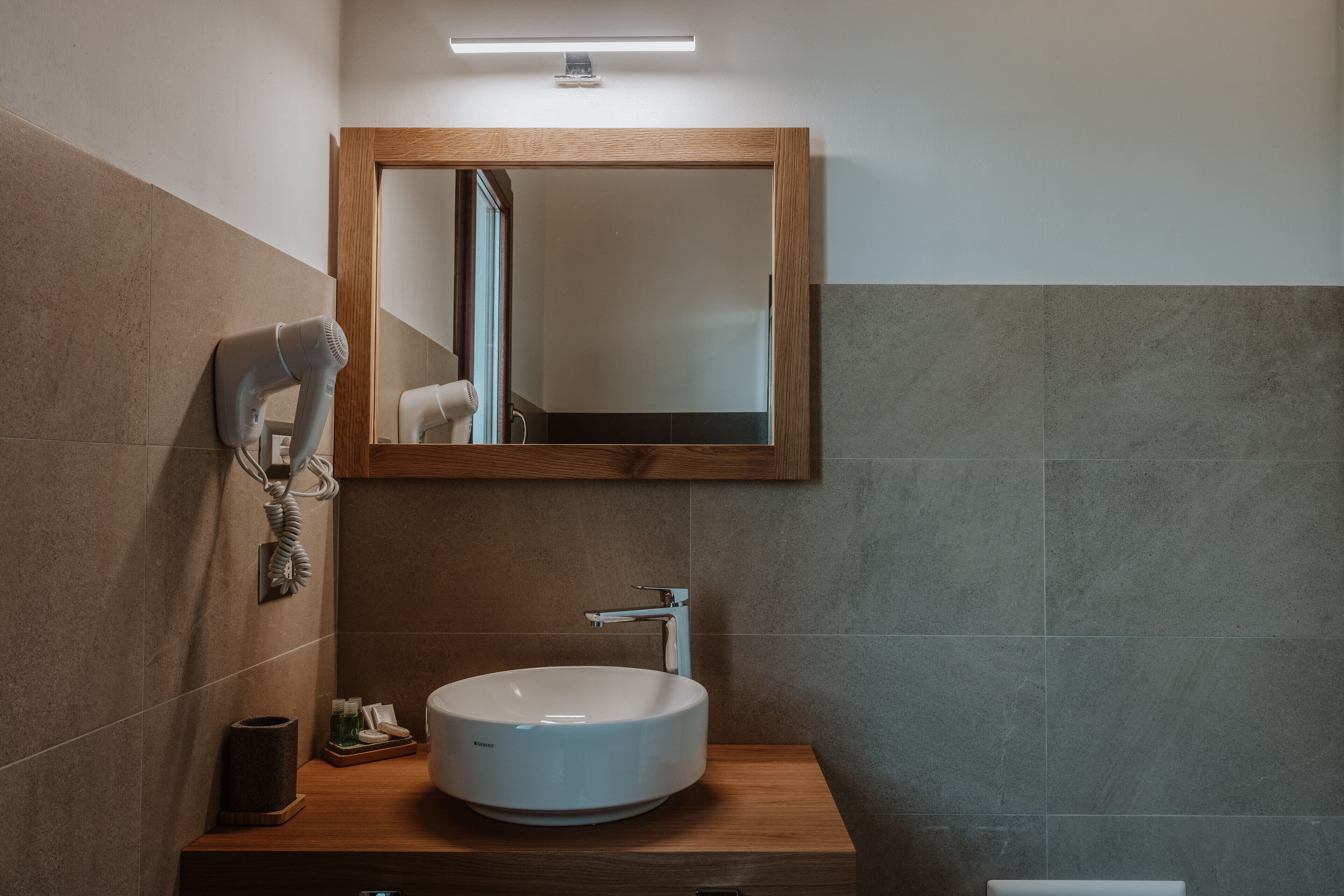 Un baño con tocador de madera, un lavamanos blanco, un espejo y un secador de pelo.