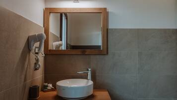 Un baño con tocador de madera, un lavamanos blanco, un espejo y un secador de pelo.