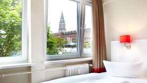 A hotel room with a bed, a window with a view of a building, and a red wall lamp. - Hotel Ostseehalle Kiel by Premiere Classe (Kiel)